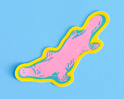 Pink platypus shaped sticker with yellow border and blue accents on a blue background.