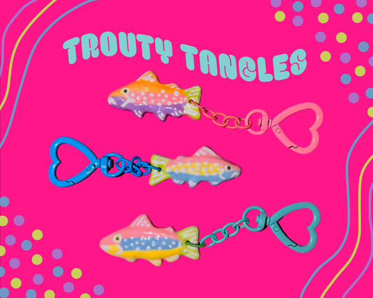 Colourful fish-shaped keychains with heart-shaped clasps on a pink background with decorative elements.