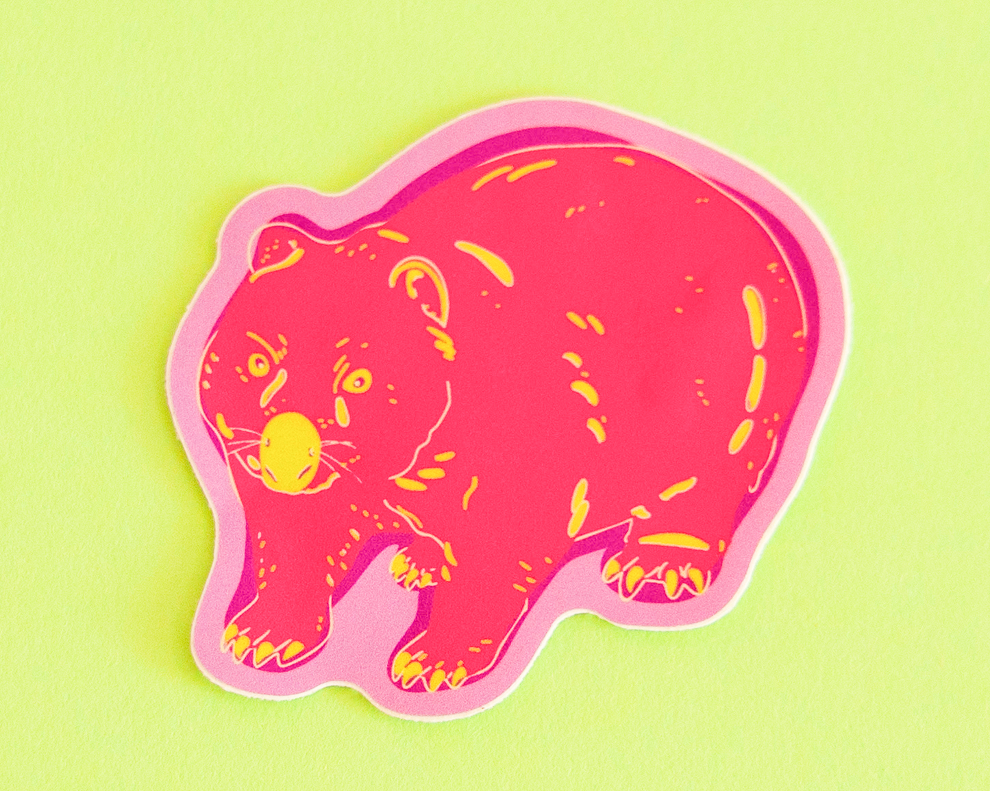 Pink wombat shaped sticker with light green markings and dark purple shadows. A light purple borders the sticker. The sticker is on a lime green background.
